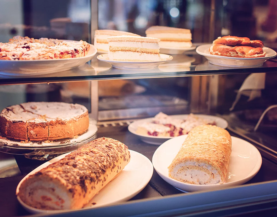 Lemp’s Genussgarten Kuchen Vitrine mit verschiedenen Kuchen und Gebäckstücken wie Blechkuchen, Sahneschnitten und Rouladen auf Tellern.